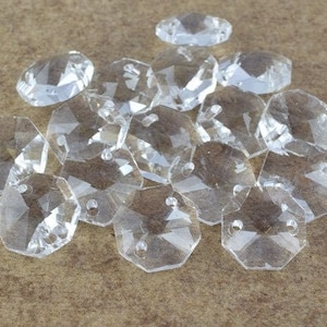May include: A group of clear glass octagonal beads with a faceted design. The beads are scattered on a brown surface.
