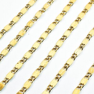 May include: Close-up of several gold-colored chain necklaces. Each chain features a repeating pattern of small, elongated oval links connected by smaller links. The chains are arranged diagonally against a white background, creating a visually appealing display.