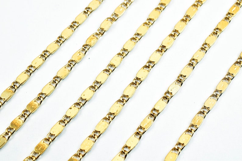May include: Close-up of several gold-colored chain necklaces. Each chain features a repeating pattern of small, elongated oval links connected by smaller links. The chains are arranged diagonally against a white background, creating a visually appealing display.