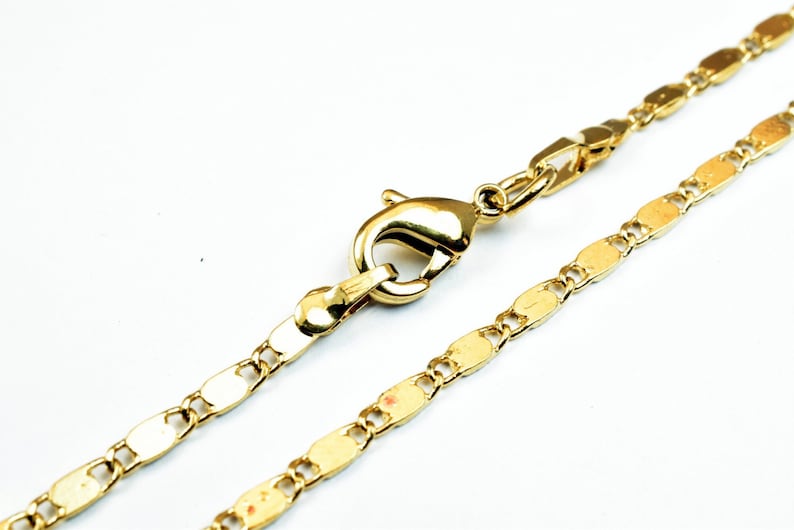 May include: A gold-colored necklace with a lobster clasp. The chain is made of small, flat, oval-shaped links. The necklace is displayed against a white background.