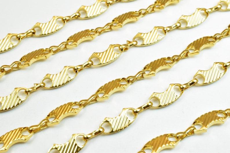 Op de afbeelding: Gouden ketting met een uniek visgraatontwerp. De ketting is gemaakt van gekoppelde, platte, ovale stukken met een getextureerd oppervlak.