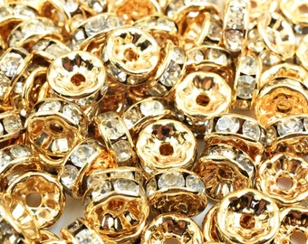 May include: A pile of gold-toned metal beads with clear crystal accents. Each bead has a round shape with a raised center and a hole in the center.