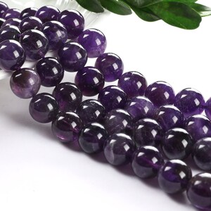 May include: A strand of round, purple amethyst beads. The beads are smooth and polished, and they have a slight sheen.