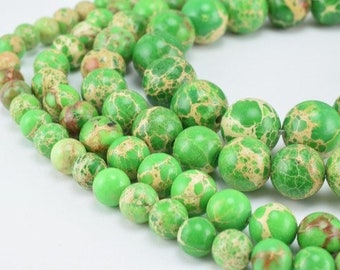 Puede incluir: Una hebra de cuentas redondas marmoleadas de color verde y blanco. Las cuentas están hechas de piedra natural y tienen un patrón moteado.