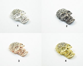 May include: Four skull-shaped charms with rhinestones. The charms are in silver, black, rose gold, and gold.