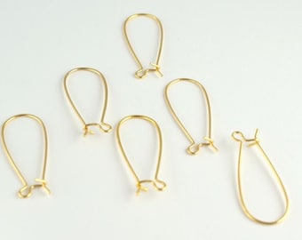 Puede incluir: Cinco ganchos para pendientes de color dorado, también conocidos como alambres para orejas, están dispuestos sobre una superficie blanca. Los ganchos son todos del mismo tamaño y forma, con un bucle en forma de lágrima y un pequeño gancho en la parte superior.