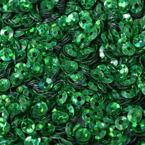 May include: A close-up of a large quantity of green iridescent sequins. The sequins are round and have a hole in the center.