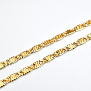 May include: A gold chain necklace with a textured, patterned design. The chain is made of interlocking oval links.