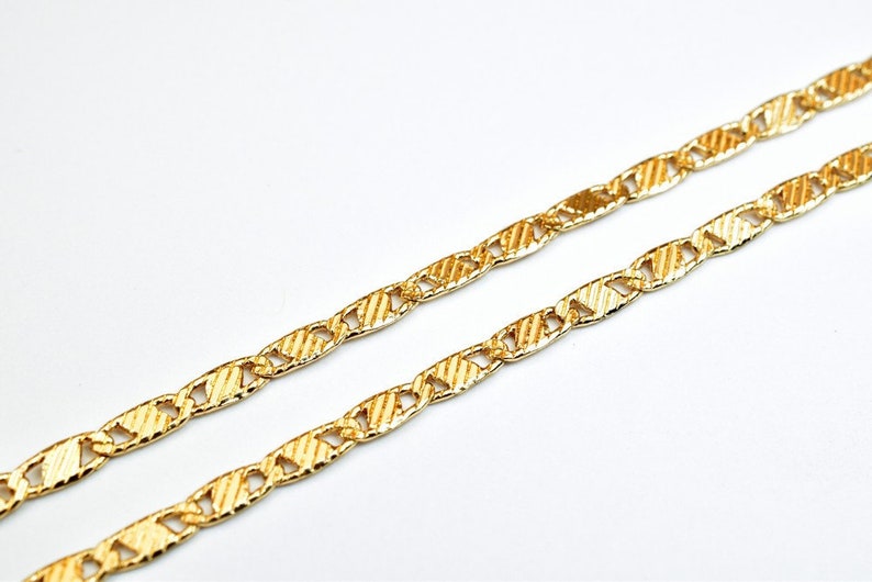 May include: A gold chain necklace with a textured, patterned design. The chain is made of interlocking oval links.