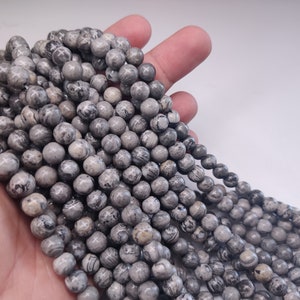 May include: A strand of gray and white round gemstone beads. The beads have a marbled pattern.