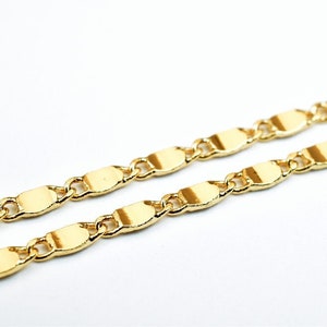 K&ouml;nnte beinhalten: Nahaufnahme einer goldfarbenen Kette. Die Kette besteht aus flachen, oval geformten Gliedern, die durch kleine, runde Glieder verbunden sind. Die Halskette ist vor einem wei&szlig;en Hintergrund platziert, was ihre gl&auml;nzende, reflektierende Oberfl&auml;che hervorhebt.
