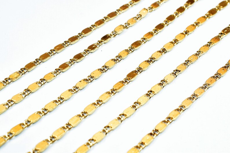 May include: Close-up of several gold-colored chain necklaces. Each chain is composed of small, elongated oval links. The chains are arranged diagonally across a white background, creating a pattern of parallel lines.