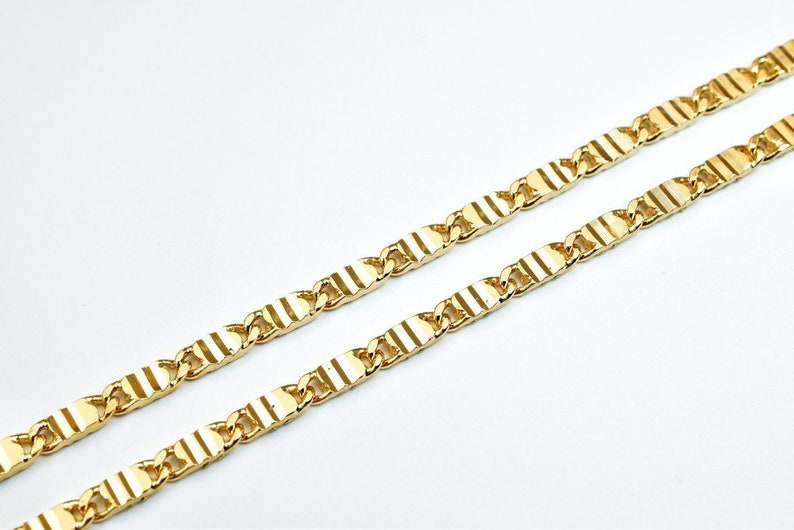 May include: A gold chain necklace with a textured, striped pattern. The chain is made of linked, rectangular pieces.