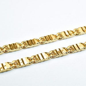 May include: A gold chain necklace with a textured, striped pattern. The chain is made of linked, rectangular pieces.