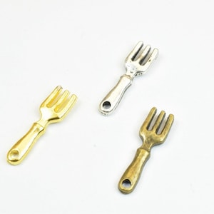 May include: Three miniature forks in different finishes: gold, silver, and bronze. The forks are about 2 inches long and have a simple design.