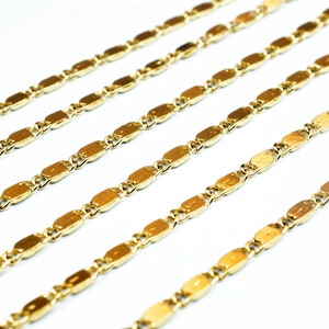 May include: Close-up of multiple gold-colored chain necklaces. Each chain features a series of elongated, oval-shaped links connected by smaller, round links. The chains are arranged diagonally against a white background.