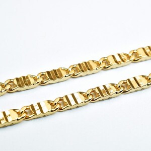 May include: A gold chain necklace with a textured, striped pattern. The chain is made of linked, rectangular pieces.