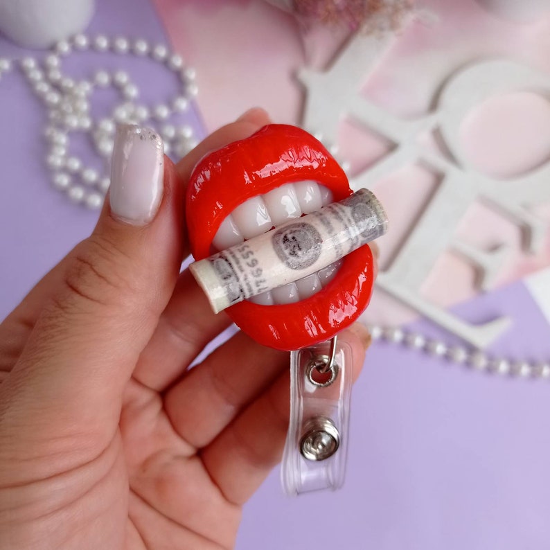 May include: Red lips with white teeth holding a rolled up dollar bill, attached to a clear plastic badge holder.