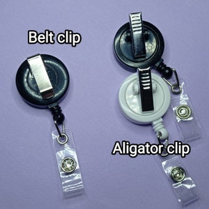 May include: Two retractable badge holders with different clips. The black holder has a belt clip and the white holder has an alligator clip. Both holders have clear plastic straps.