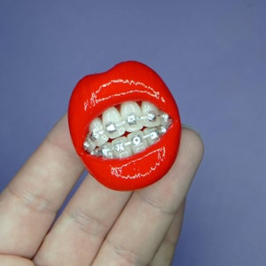 May include: A red, glossy, sculpted mouth with white teeth and silver braces.