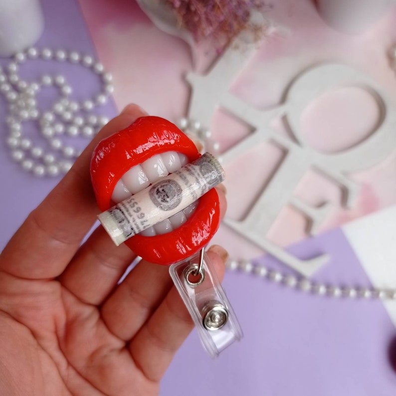 May include: Red lips with white teeth holding a rolled up dollar bill. The lips are attached to a clear plastic retractable badge holder.