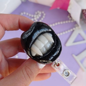 Pu&ograve; includere: Portabadge a forma di bocca di vampiro nero e bianco con un clip in plastica trasparente.