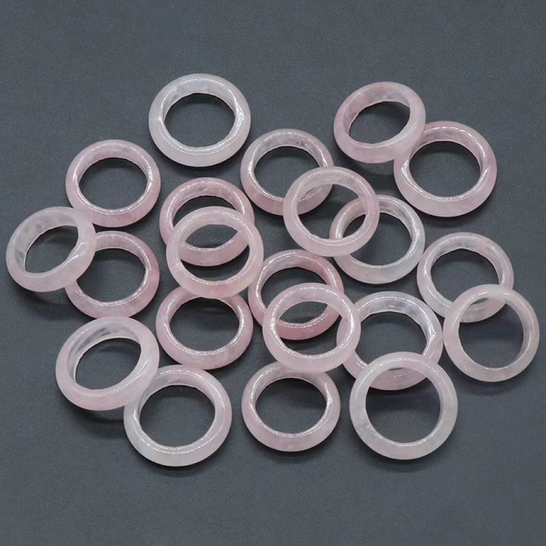 May include: A collection of 18 pale pink gemstone rings. The rings are made of smooth, polished stone and are all the same size.