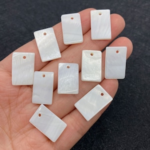 以下が含まれることがあります： 吊り下げ用の穴が上部に開いた、白い長方形の真珠貝のチャームが10個です。