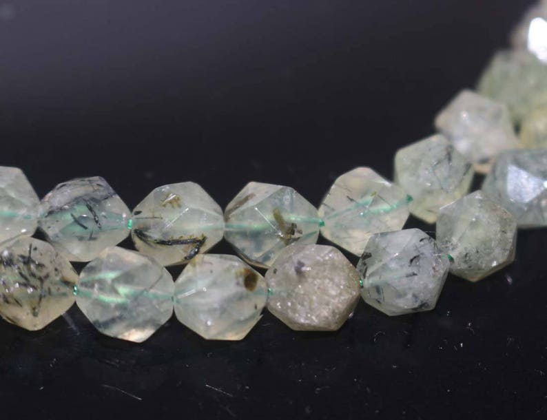 May include: A strand of faceted, translucent green and black gemstone beads. The beads are irregularly shaped and have a rough, natural texture.