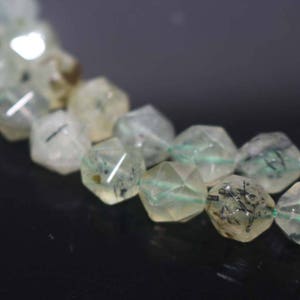 May include: A strand of faceted, translucent green beads with black inclusions. The beads are strung on a clear elastic cord.