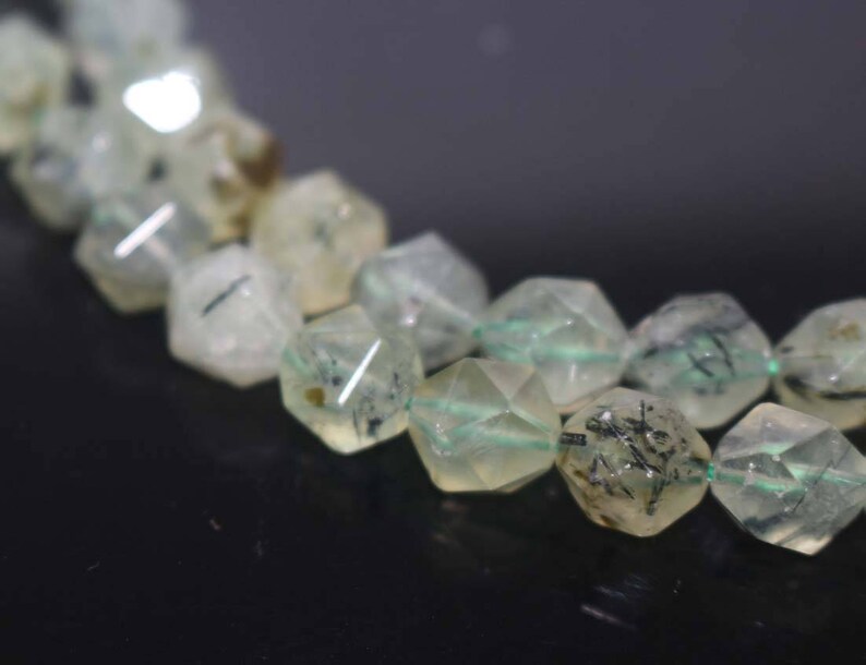 May include: A strand of faceted, translucent green beads with black inclusions. The beads are strung on a clear elastic cord.