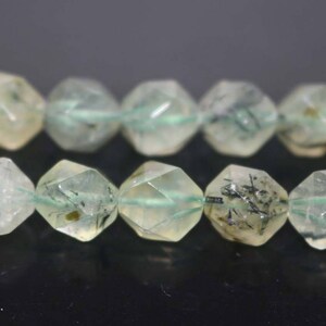 May include: A strand of faceted green and black gemstone beads. The beads are translucent and have a speckled appearance.