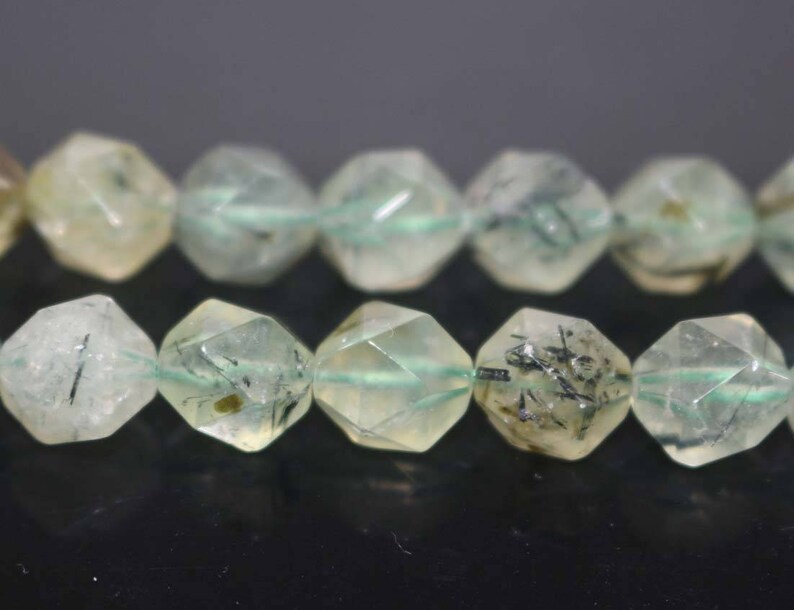 May include: A strand of faceted green and black gemstone beads. The beads are translucent and have a speckled appearance.