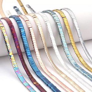 Peut inclure: Plusieurs colliers à maillons rectangulaires plats aux finitions métalliques variées. Les colliers présentent des nuances d'or, d'argent, de bleu et des couleurs irisées. Les bijoux sont présentés sur une surface blanche.