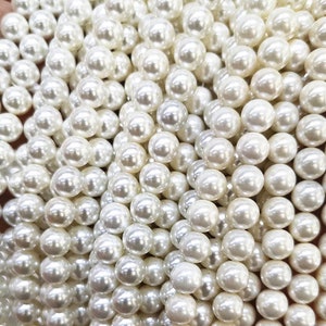 May include: A close-up of a pile of white pearl beads. The beads are round and smooth, and they are all the same size.