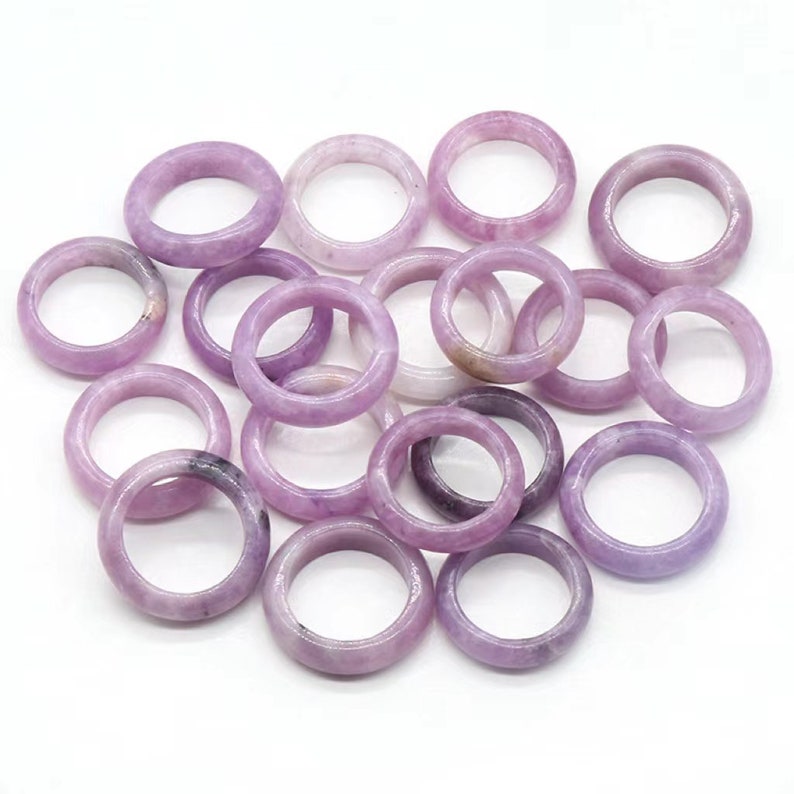 May include: A pile of 15 lavender-colored gemstone rings. The rings are smooth and polished, and they are all about the same size.