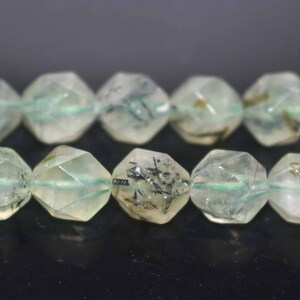May include: A strand of faceted green and black gemstone beads. The beads are faceted and have a starburst shape. The beads are strung on a clear elastic cord.