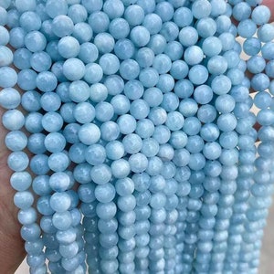 Könnte beinhalten: Stränge aus hellblauen, runden Edelsteinperlen. Die Perlen haben eine glatte, polierte Oberfläche und sind aufgefädelt. Die Farbe ist ein weiches, helles Blau, das an Aquamarin erinnert. Geeignet für die Schmuckherstellung.