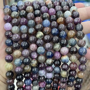 Puede incluir: Una hebra de cuentas redondas de piedras preciosas multicolores. Las cuentas son una mezcla de azul, morado, rosa y marrón. Las cuentas son todas aproximadamente del mismo tamaño y están enhebradas en un hilo transparente.