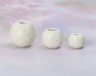 Peut inclure: Trois perles en céramique blanche avec une texture mouchetée. Les perles sont de tailles différentes, la plus grande à l'arrière et la plus petite à l'avant.