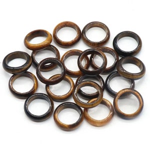 May include: A group of 18 brown and gold tiger's eye stone rings. The rings are all the same size and shape, and they are arranged in a pile.