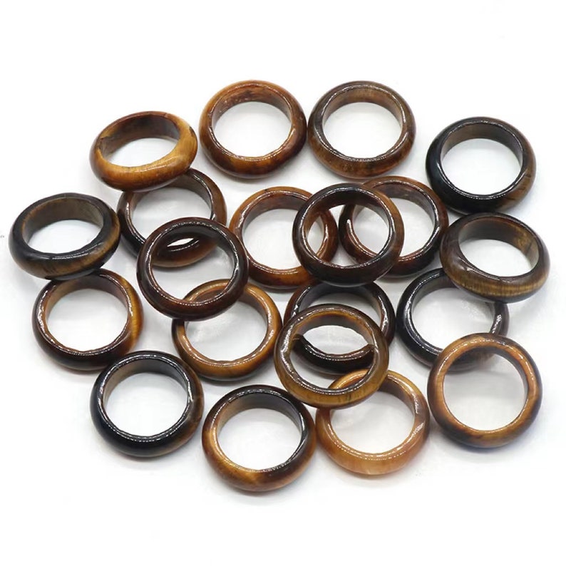 May include: A group of 18 brown and gold tiger's eye stone rings. The rings are all the same size and shape, and they are arranged in a pile.