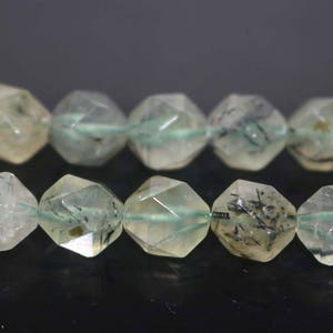 May include: A strand of faceted green and clear quartz beads with black inclusions. The beads are strung on a green thread.