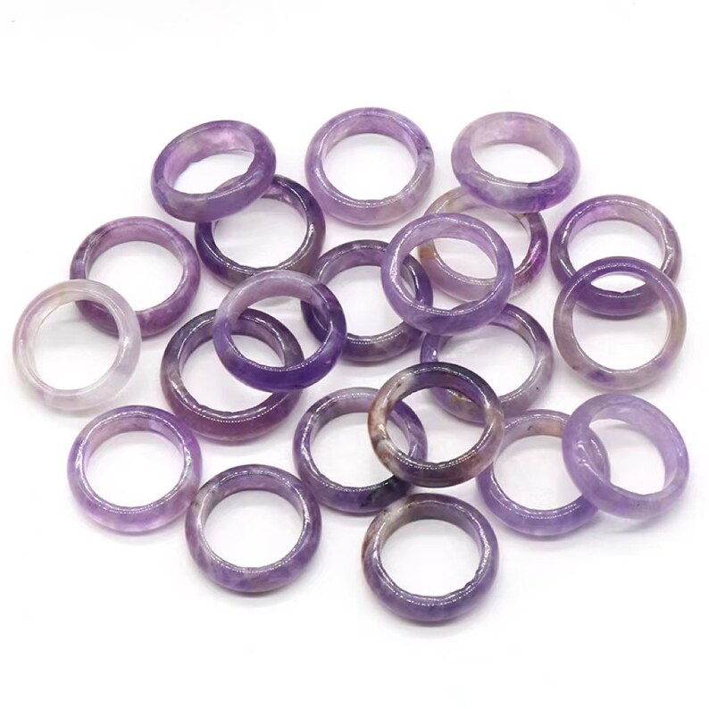 May include: A collection of amethyst gemstone rings, each ring is a different shade of purple, the rings are smooth and polished.