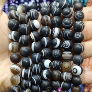 May include: A strand of black and white agate beads. The beads are round and have a polished finish. The agate has a natural pattern of white and black stripes.