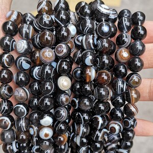 May include: A strand of black and white agate beads with intricate patterns. The beads are round and smooth, and they are strung together on a clear thread.