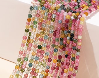 May include: A strand of multi-colored gemstone beads, featuring shades of pink, green, yellow, and blue. The beads are round and smooth, and they are strung together on a clear thread.