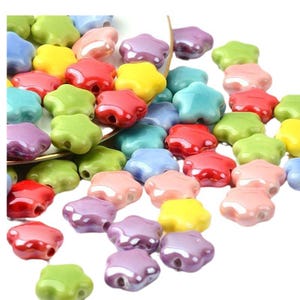 May include: A collection of colorful star-shaped ceramic beads. The beads are in various shades of red, green, blue, yellow, pink, and purple. They have a glossy finish and a hole in the center for stringing.