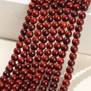 May include: A strand of dark red wooden beads. The beads are round and smooth, and they are strung together on a thin cord. The beads are arranged in a staggered pattern, creating a visually appealing design.
