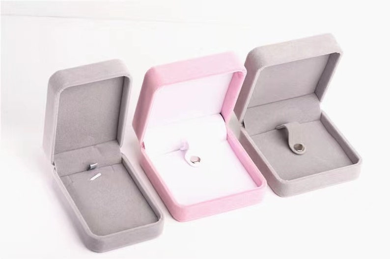 May include: Three open jewelry boxes in a row, each with a different color scheme. The boxes are rectangular with rounded edges and a hinged lid. The box on the left and right are gray, while the center box is pink.